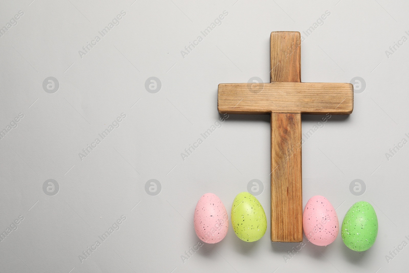 Photo of Wooden cross and painted Easter eggs on light grey background, flat lay. Space for text