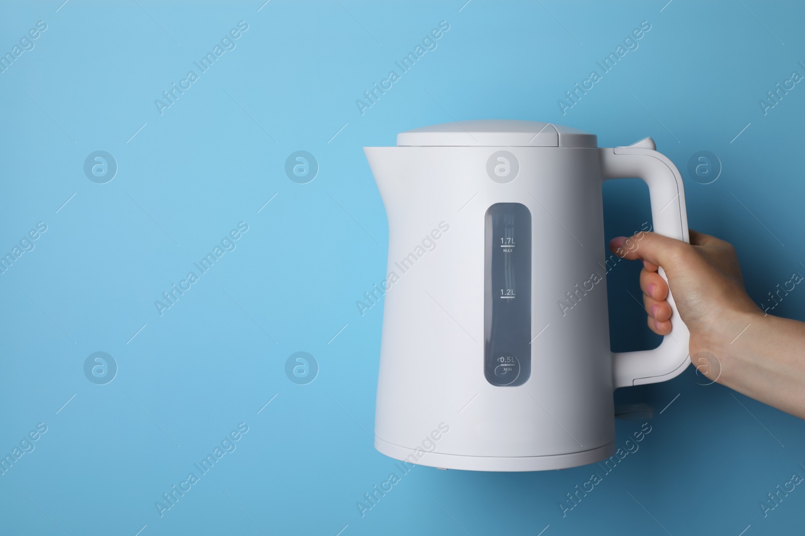 Photo of Woman holding modern electric kettle on light blue background, closeup. Space for text