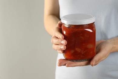 Woman holding jar of canned lecho on light background, closeup. Space for text