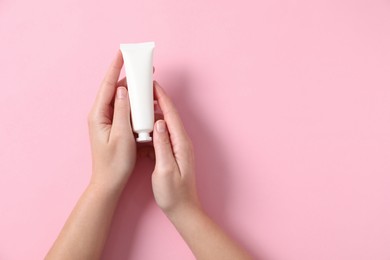 Woman with tube of hand cream on pink background, top view. Space for text