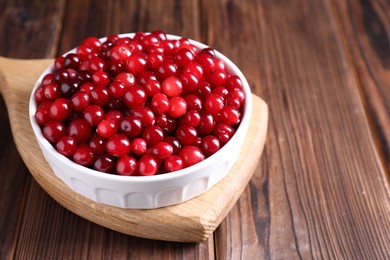 Photo of Fresh ripe cranberries in bowl on wooden table, closeup