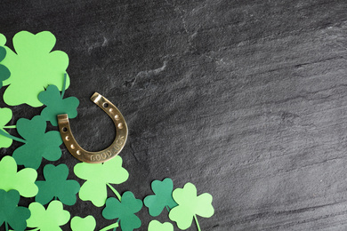 Photo of Flat lay composition with clover leaves and horseshoe on black stone background, space for text. St. Patrick's day