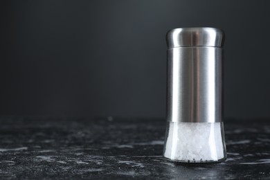 Photo of Salt shaker on dark marble table, closeup. Space for text