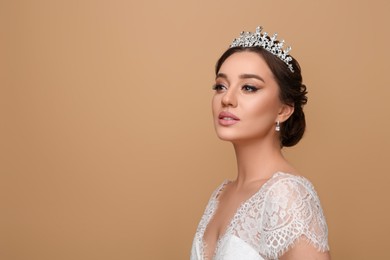 Beautiful young woman wearing luxurious tiara on beige background, space for text