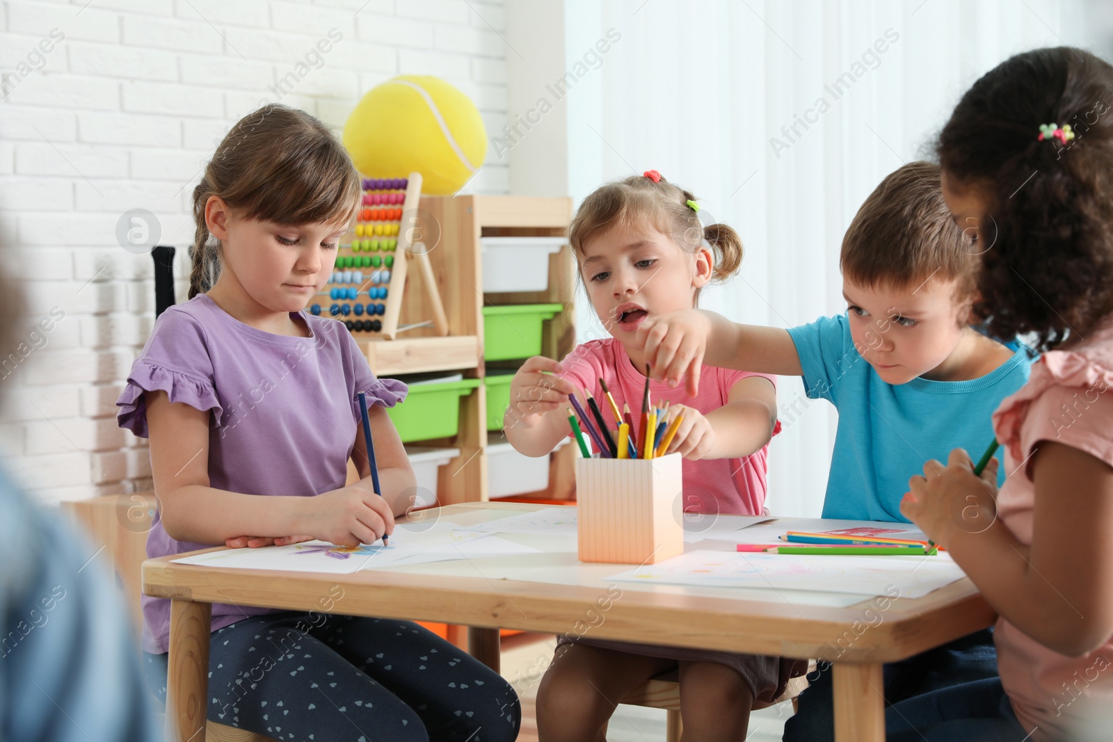 Photo of Adorable children drawing together at table indoors. Kindergarten playtime activities