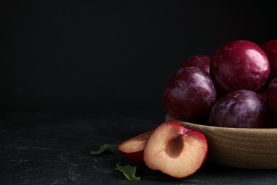 Delicious ripe plums in wooden bowl on black table. Space for text