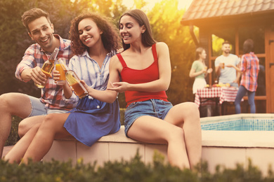 Image of Happy friends with drinks at barbecue party near swimming pool outdoors on sunny day