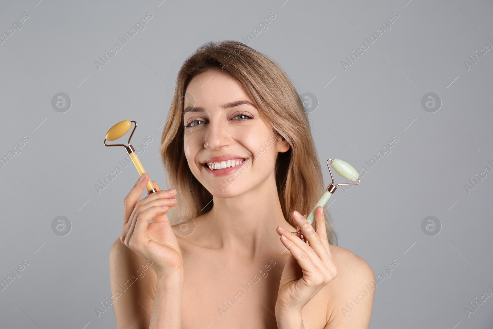 Photo of Young woman with natural jade face rollers on light grey background