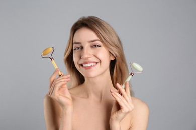 Photo of Young woman with natural jade face rollers on light grey background