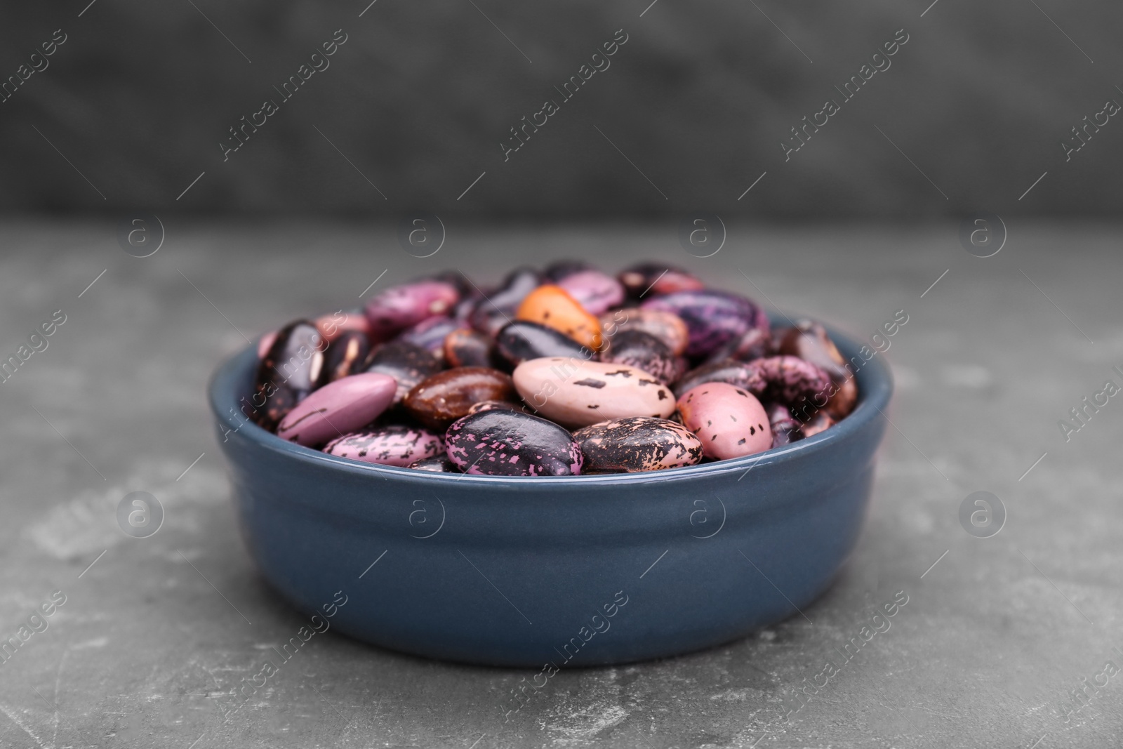 Photo of Bowl with dry kidney beans on grey table, closeup