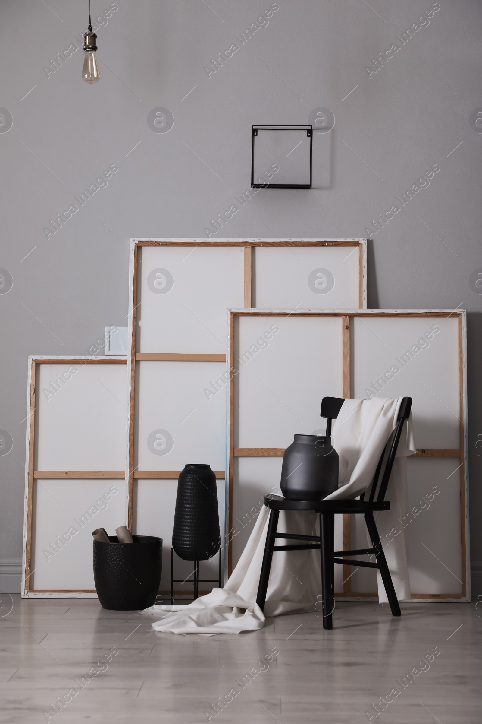 Photo of Chair with white fabric, vases and paintings near grey wall in artist's studio