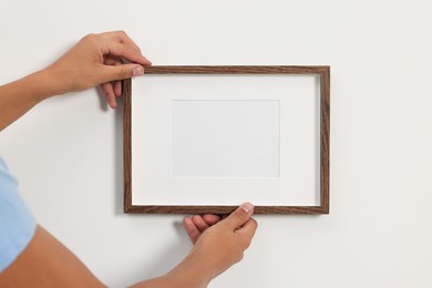 Young man hanging picture frame on white wall indoors, closeup