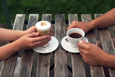 Photo of Man and woman drinking coffee at wooden table in outdoor cafe, closeup