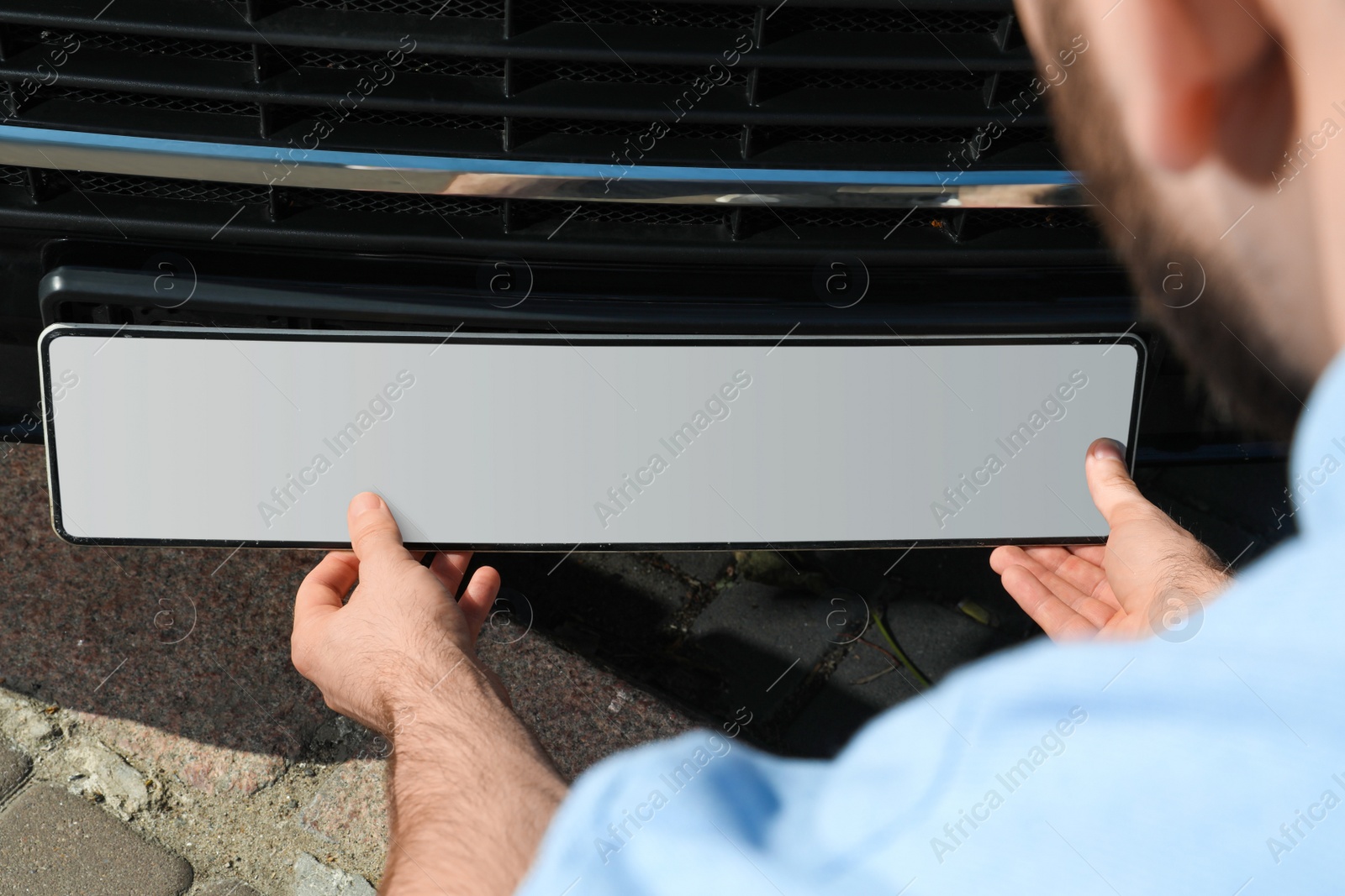 Photo of Man installing vehicle registration plate outdoors, closeup