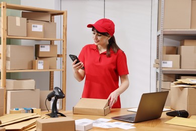 Photo of Parcel packing. Post office worker with smartphone and box indoors