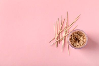 Wooden toothpicks and holder on pink background, flat lay. Space for text