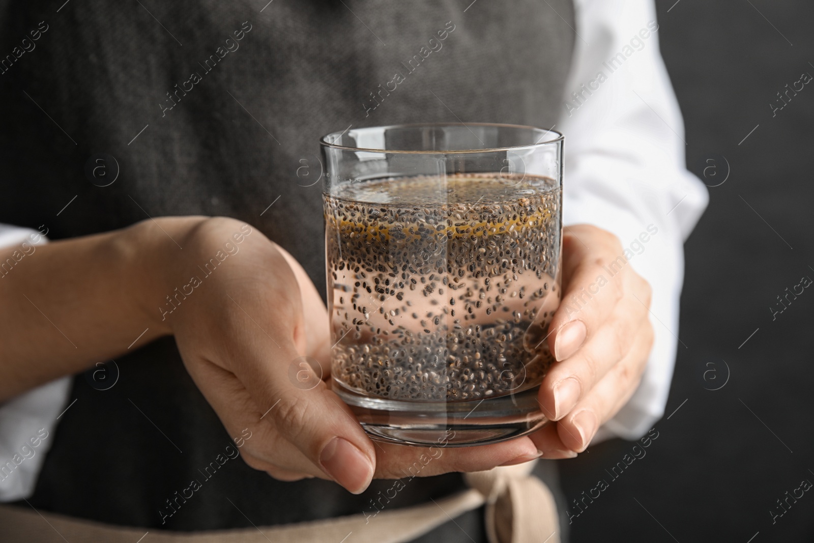 Photo of Woman holding glass of water with chia seeds on black background, closeup