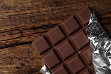 Photo of Tasty milk chocolate bar wrapped in foil on wooden table, top view