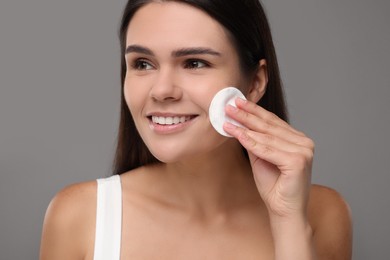 Photo of Young woman cleaning her face with cotton pad on grey background, closeup