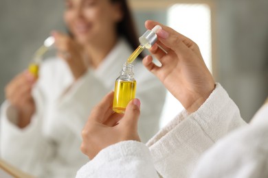 Young woman with cosmetic serum in her hands indoors, closeup