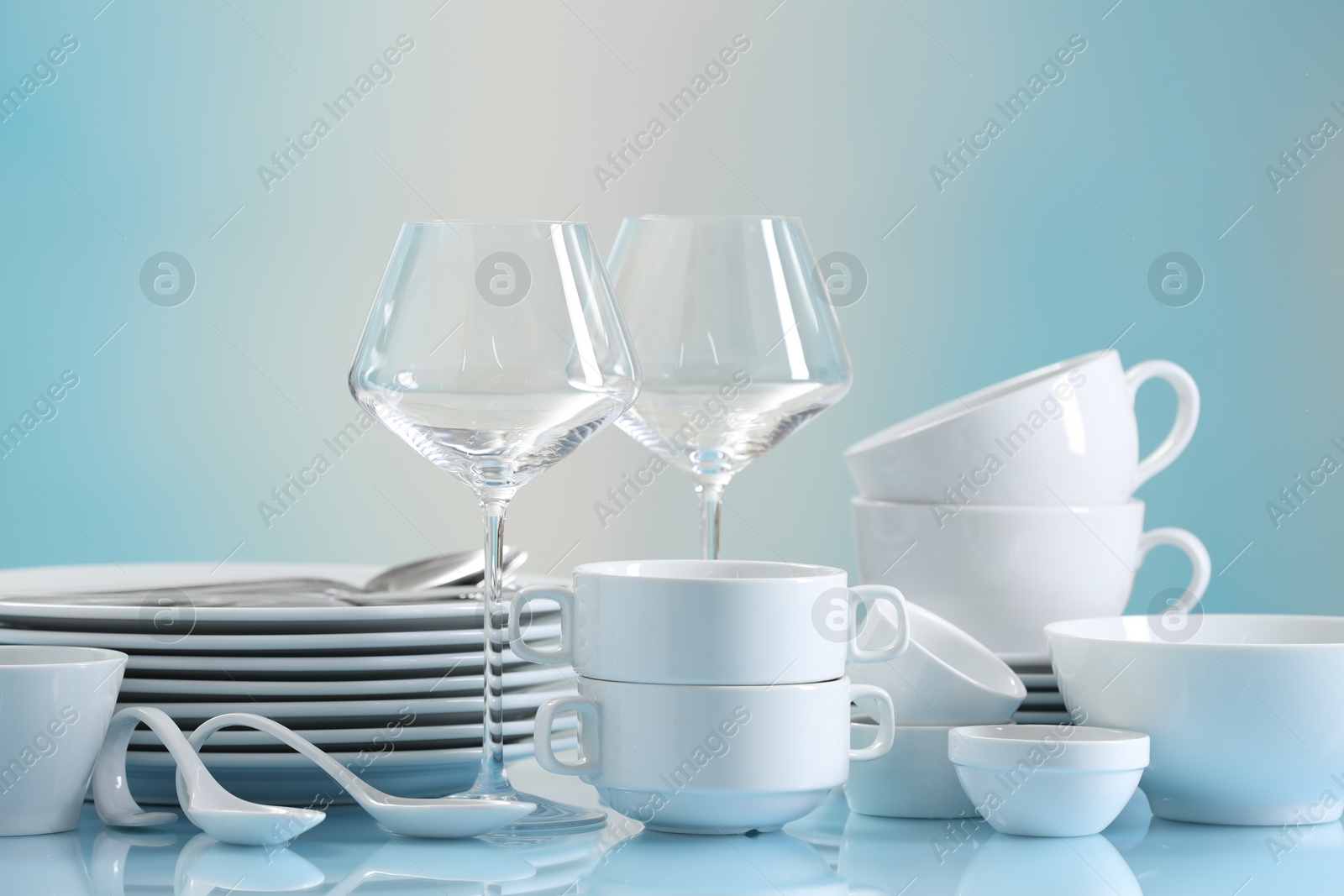 Photo of Set of many clean dishware and glasses on light blue table