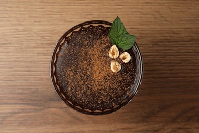 Photo of Dessert bowl of delicious hot chocolate with hazelnuts and fresh mint on wooden table, top view