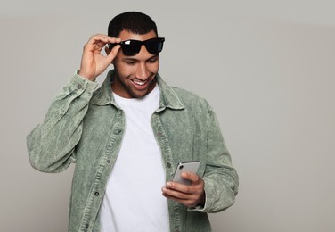 Photo of Smiling African American man in sunglasses with smartphone on light grey background. Space for text