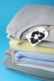 Photo of Stack of clothes with recycling label on light blue background, closeup