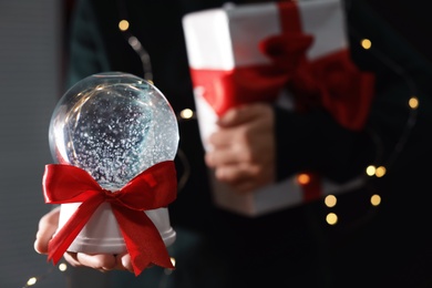 Woman holding Christmas snow globe on blurred background, closeup. Space for text