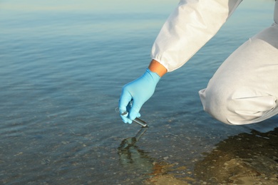 Scientist with test tube taking sample from river for analysis, closeup