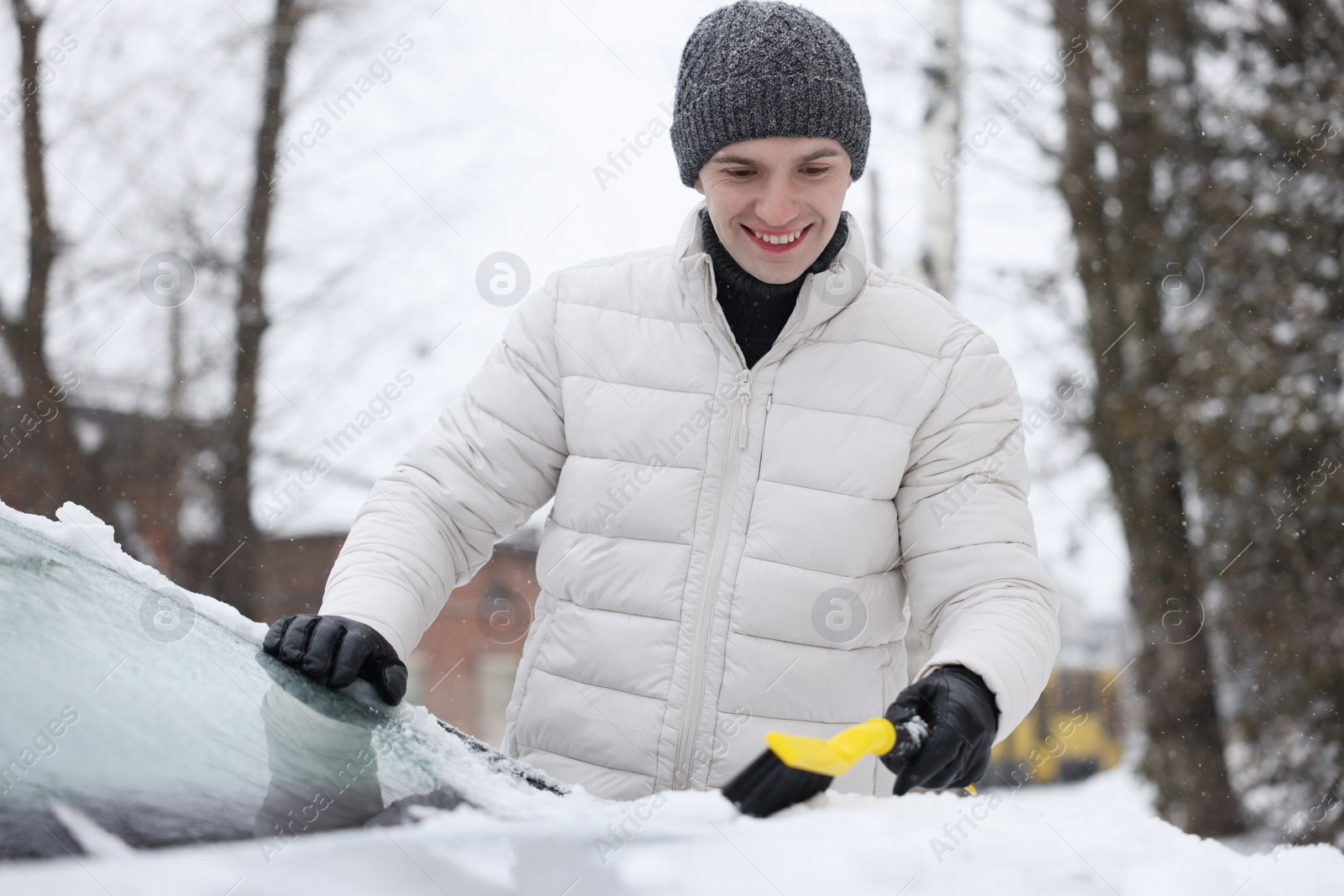 Photo of Man cleaning snow from car hood outdoors