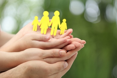 Parents and kid holding paper cutout of family in hands outdoors, closeup