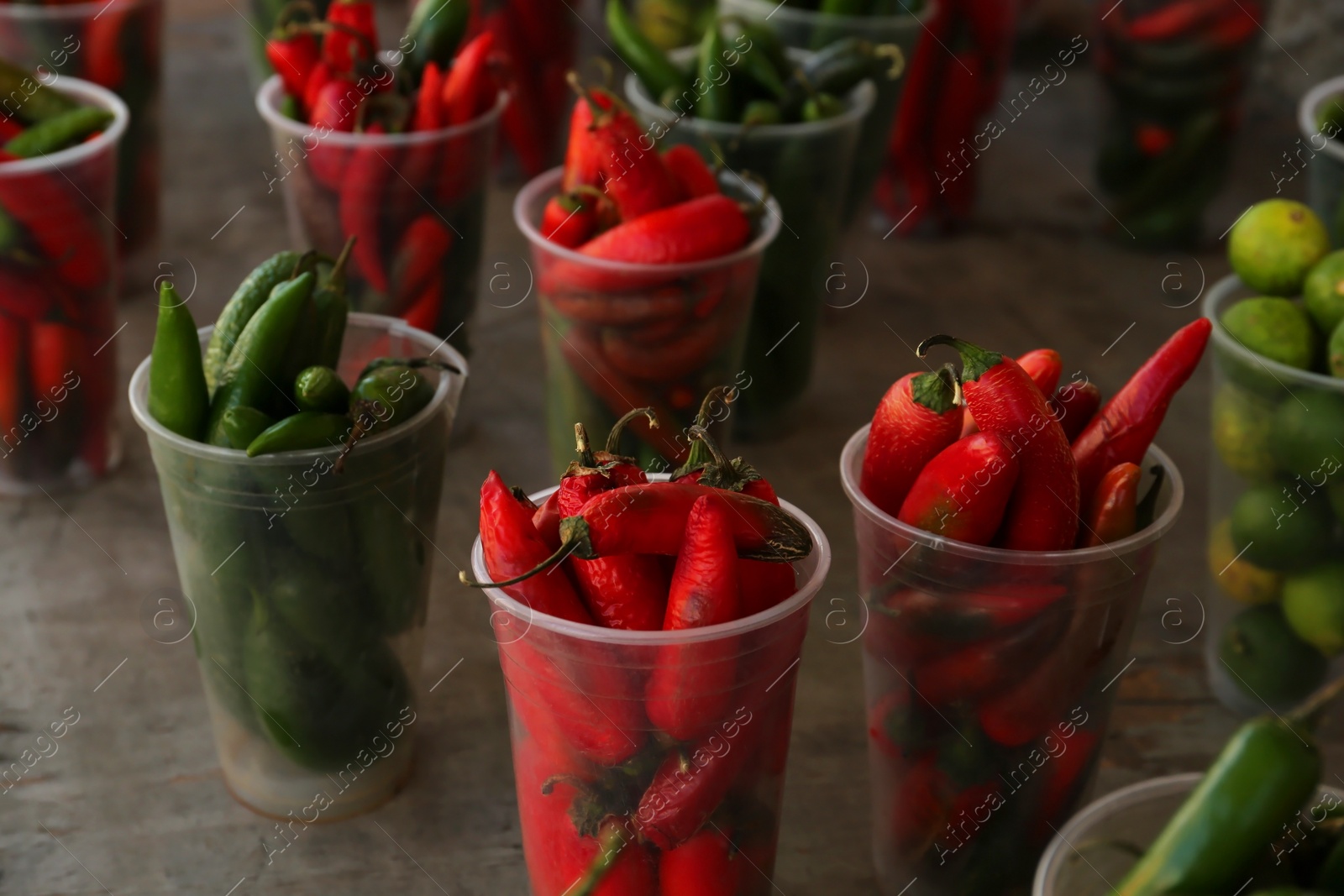Photo of Many plastic cups with fresh chilli peppers on grey counter at market, closeup