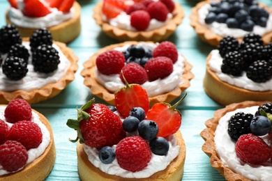 Photo of Many different berry tarts on blue wooden table. Delicious pastries