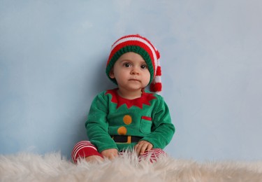 Photo of Cute baby wearing elf costume on fluffy carpet near light blue wall. Christmas celebration