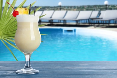 Image of Tasty Pina Colada cocktail on blue wooden table near outdoor swimming pool, space for text