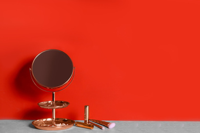 Photo of Small mirror and makeup products on grey marble table near red wall. Space for text