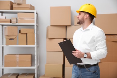 Young man with clipboard near cardboard boxes at warehouse