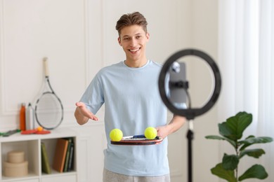 Photo of Smiling sports blogger with tennis racket and balls streaming online fitness lesson at home