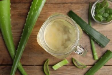 Photo of Fresh aloe drink in mason jar and leaves on wooden table, flat lay