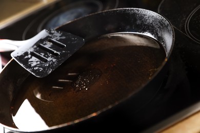 Photo of Frying pan with spatula and used cooking oil on stove, closeup