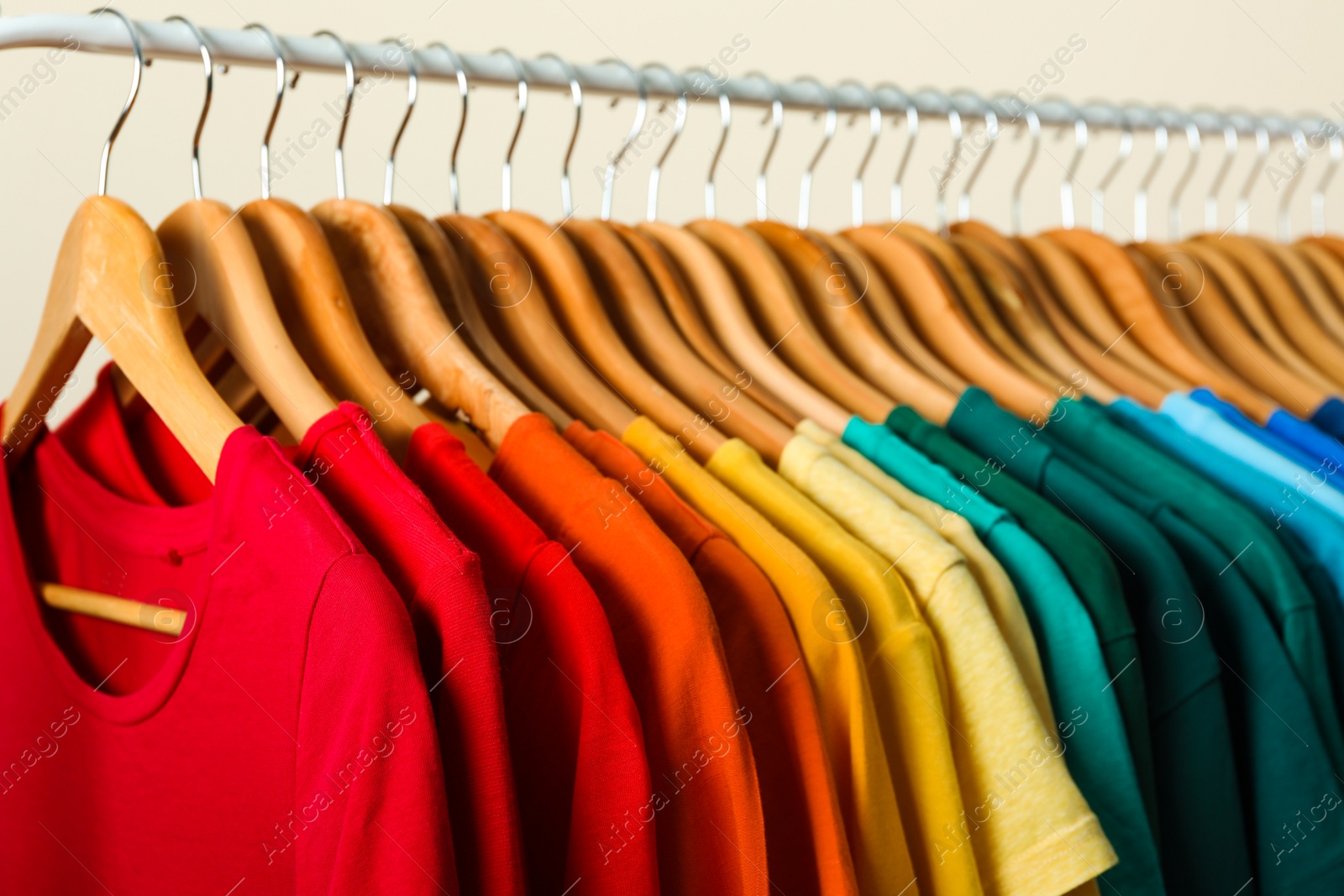 Photo of Rack with bright clothes on light background. Rainbow colors