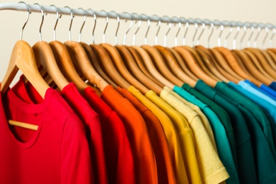 Photo of Rack with bright clothes on light background. Rainbow colors