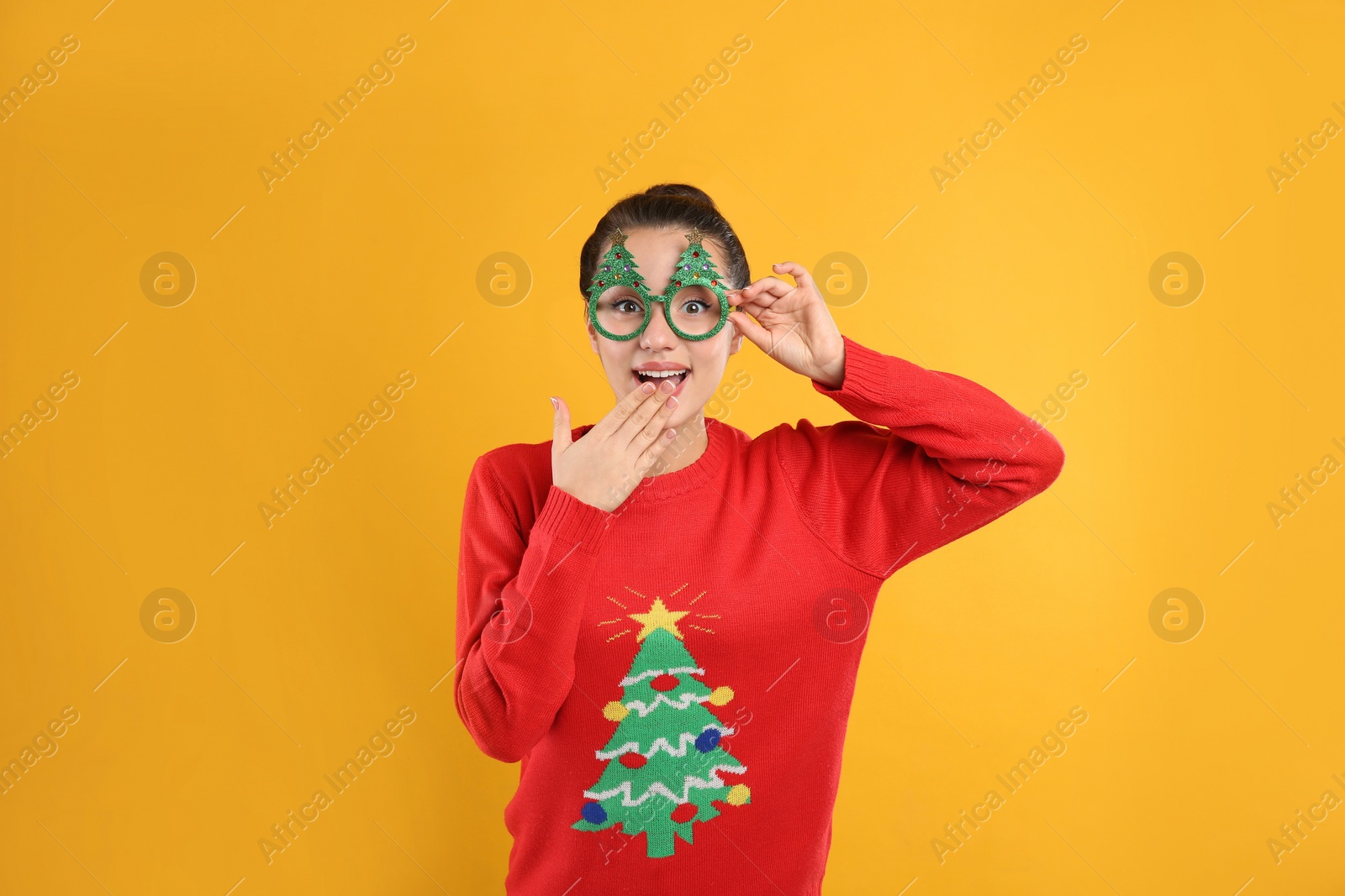 Photo of Young woman in Christmas sweater and party glasses on yellow background