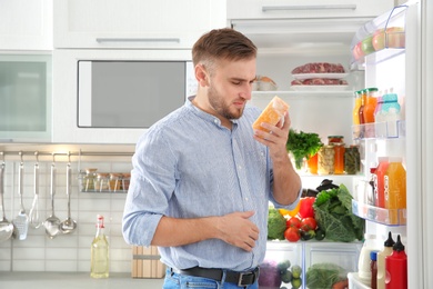 Photo of Man feeling bad smell from stale cheese near refrigerator at home