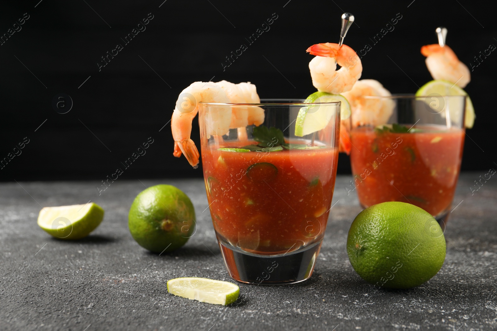 Photo of Tasty shrimp cocktail with sauce in glasses and limes on grey textured table, space for text