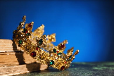 Photo of Beautiful golden crown and old books on dark blue background, space for text. Fantasy item