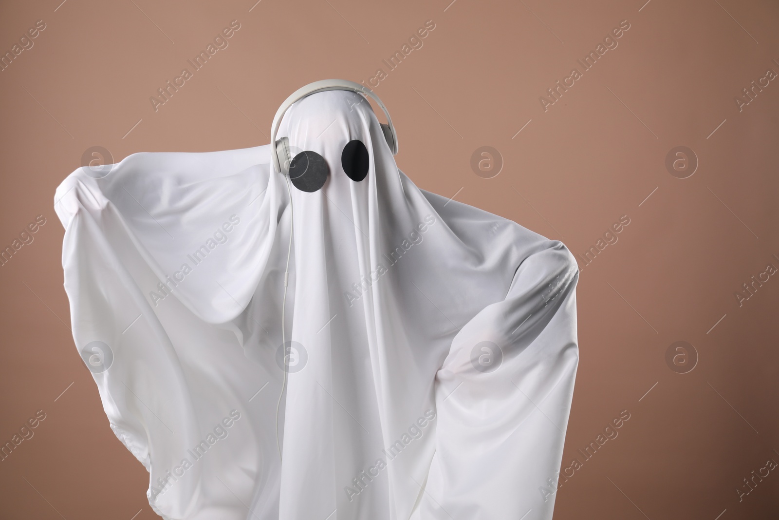 Photo of Person in ghost costume with headphones on dark beige background, space for text