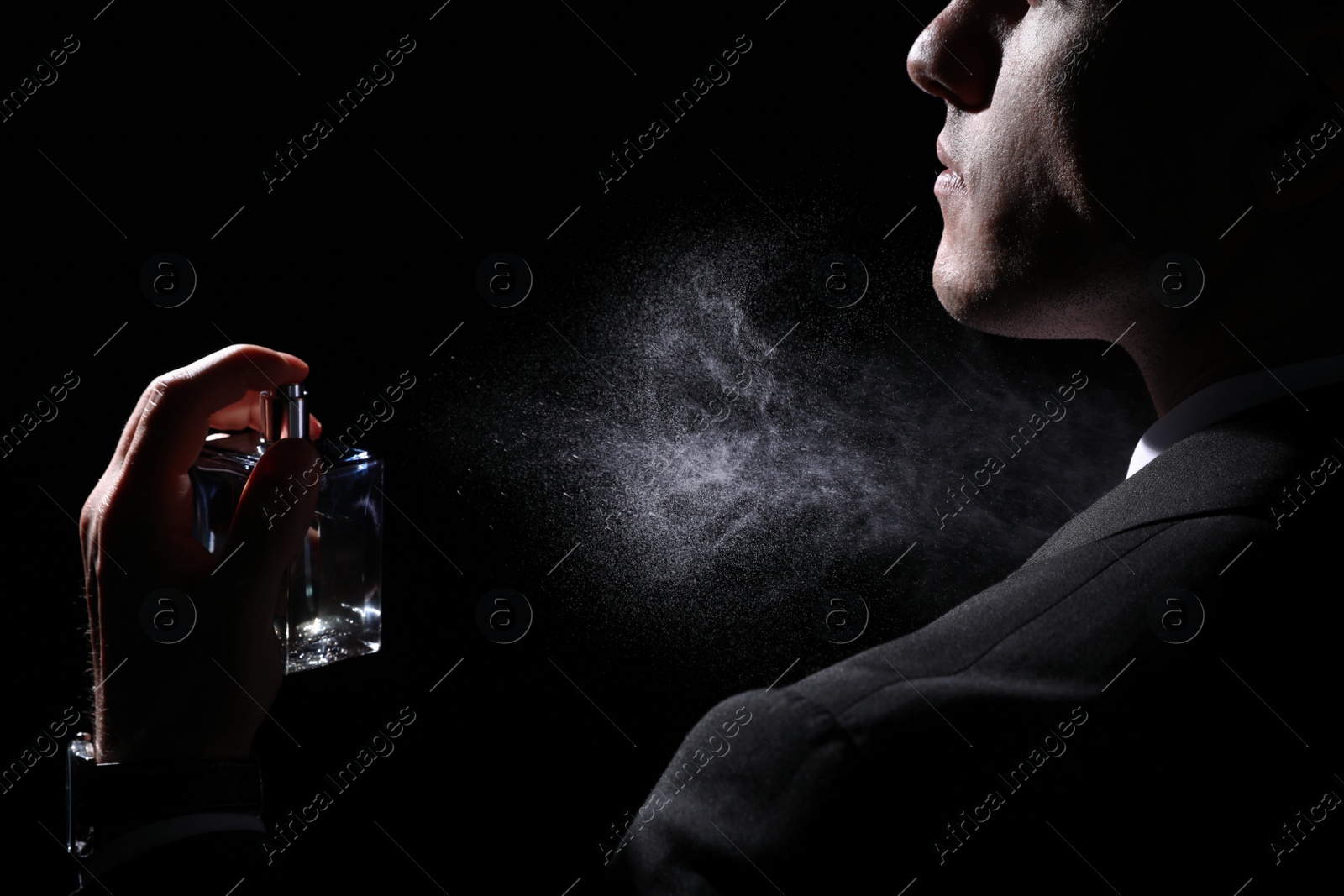 Photo of Man spraying luxury perfume on black background, closeup