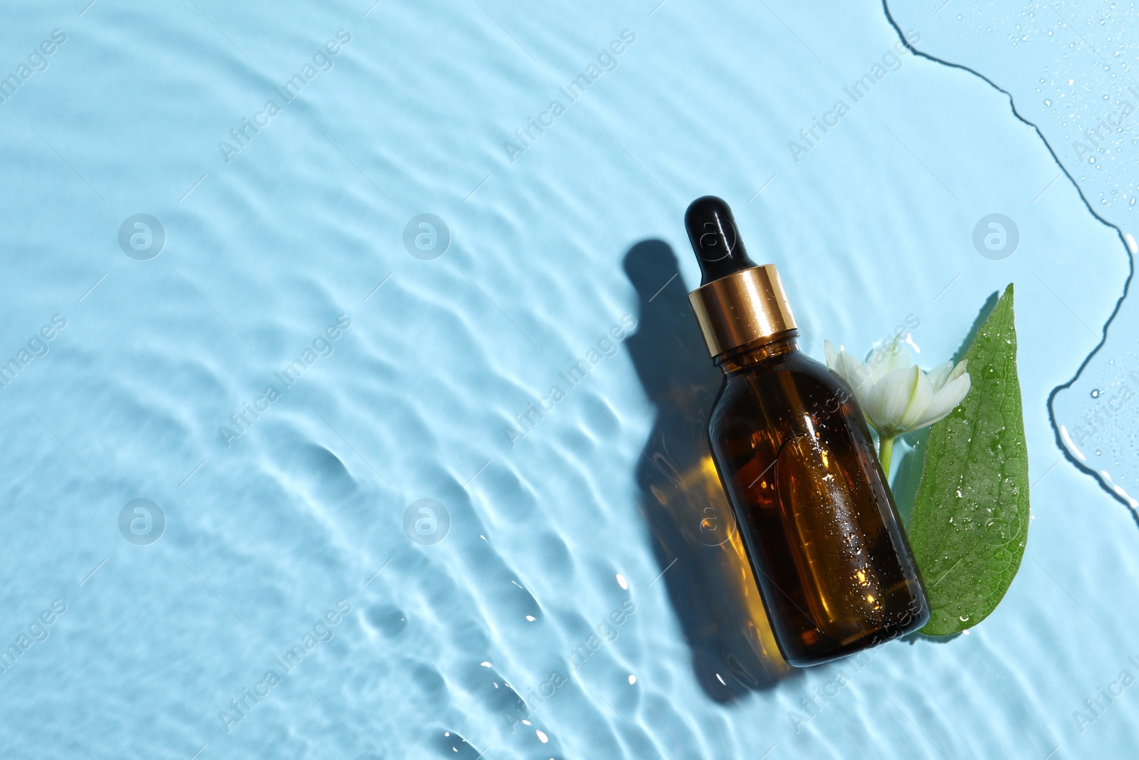 Photo of Bottle of cosmetic oil, green leaf and flower in water on light blue background, flat lay. Space for text